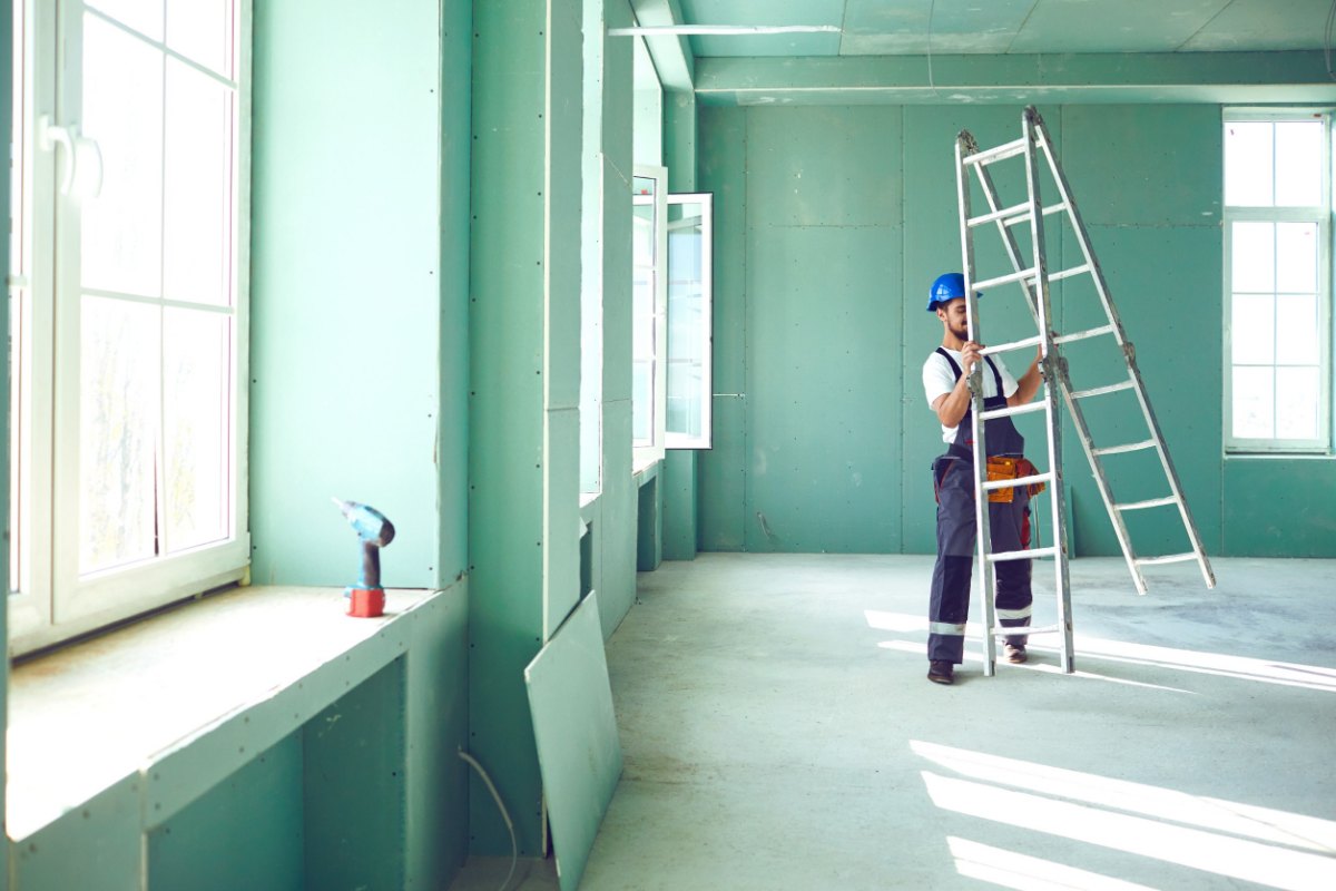 Fondo azul con hombre levantando una escalera en una casa en obras